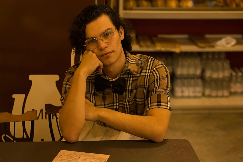 a man sitting at a table with his hand on his chin, an album cover, pexels, fantastic realism, non binary model, in classic diner, stranger things character, bella poarch