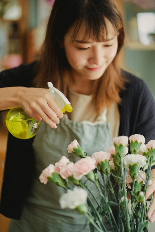 a woman standing in front of a vase filled with flowers, spraying liquid, carefully crafted, helpful, carnation