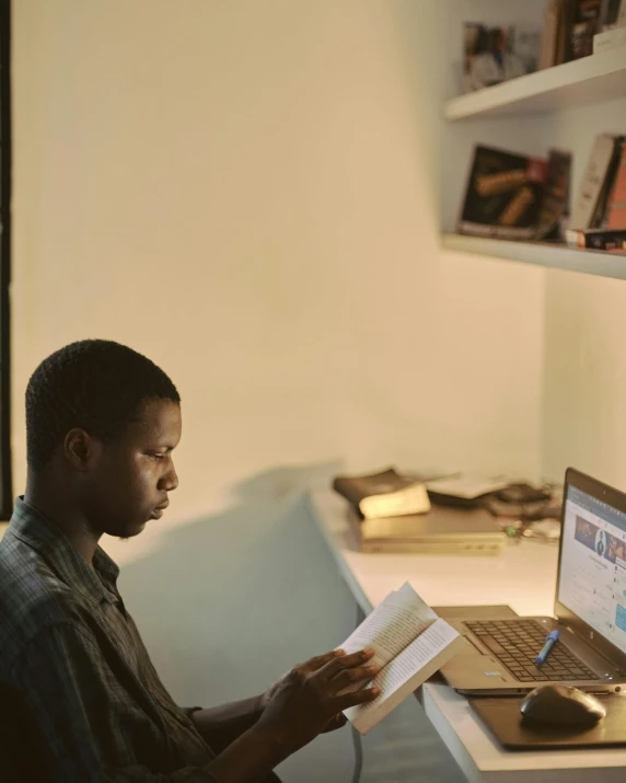 a man sitting at a desk reading a book, trending on unsplash, black teenage boy, bisexual lighting, laptops, wide film still