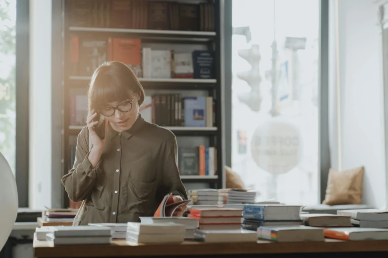 a woman sitting at a table talking on a cell phone, filled with books, top selection on unsplash, bookshops, avatar image