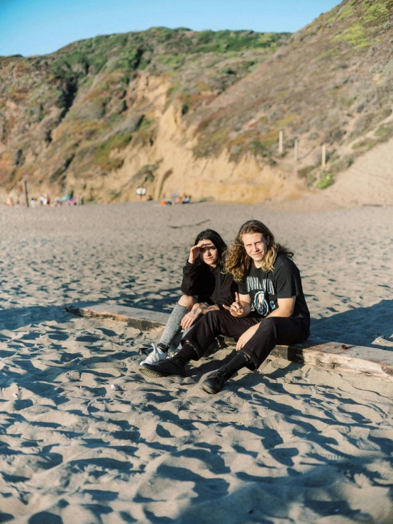 a couple of people sitting on top of a sandy beach, posing for a picture, ville valo, non-binary, bay area