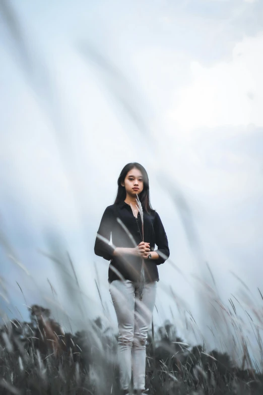 a woman standing in a field of tall grass, a portrait, by Basuki Abdullah, unsplash, art photography, wearing a black jacket, sky swirling with black wind, ((portrait)), handsome girl