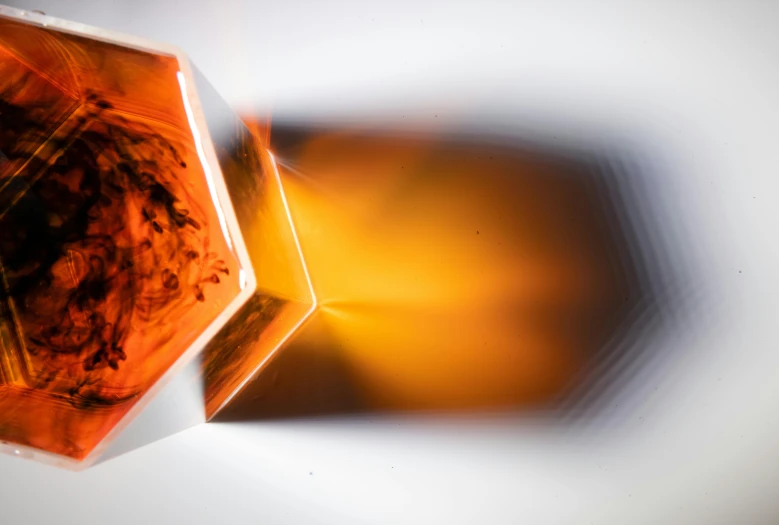 a close up of a glass object on a table, an abstract sculpture, by Adam Marczyński, unsplash, liquid translucent amber, cubic minerals, coloured in orange fire, hexagonal shaped