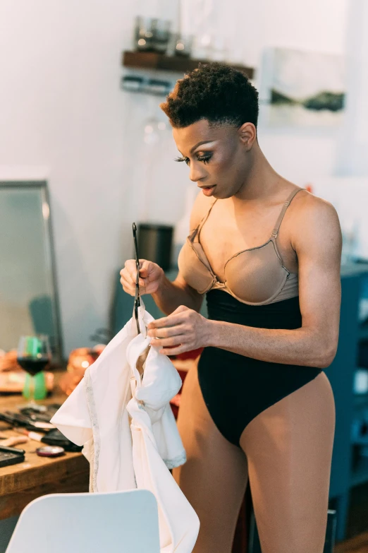 a woman in a bathing suit standing next to a desk, by William Berra, trending on pexels, ru paul\'s drag race, putting makeup on, vests and corsets, androgynous male