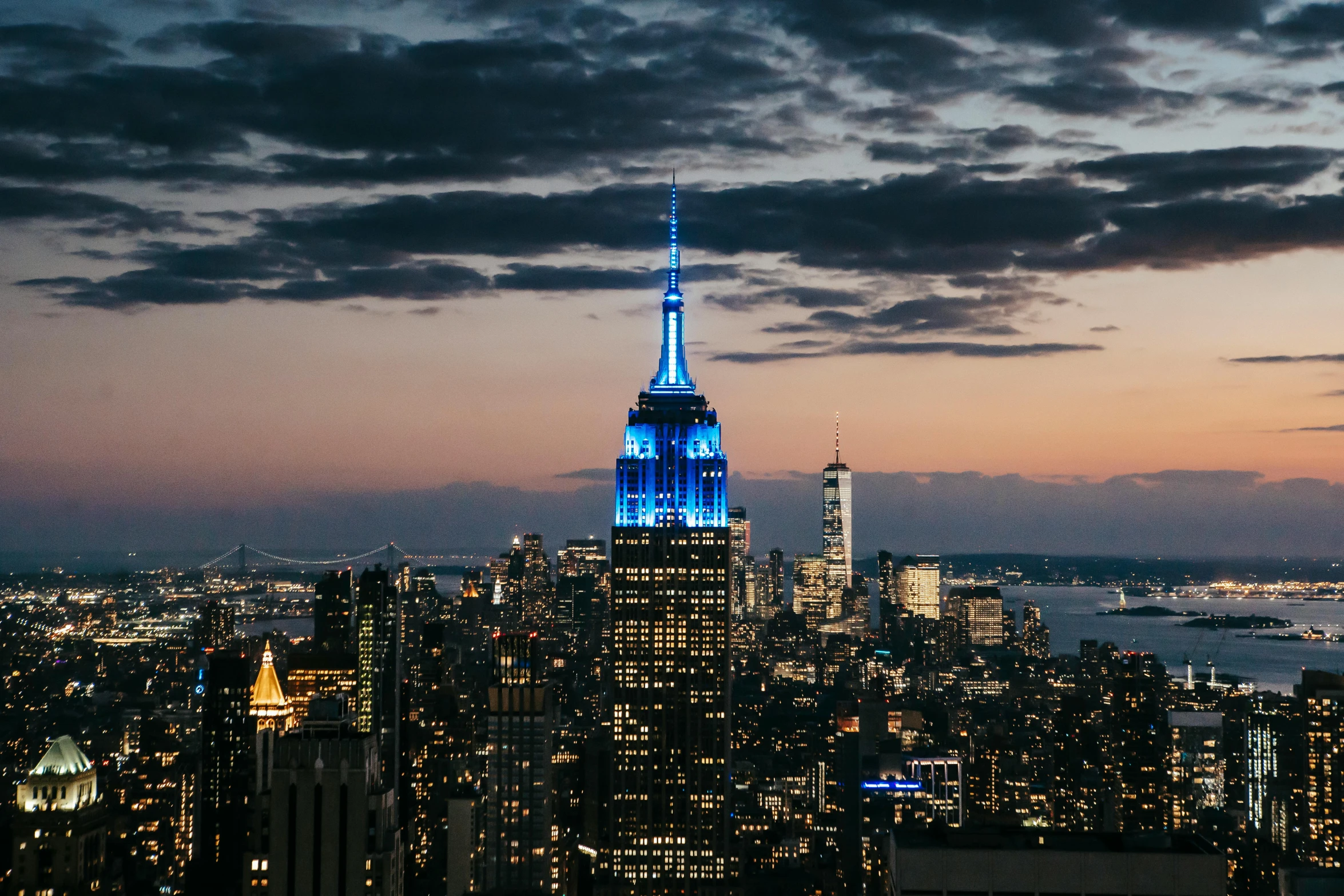 the empire state building lit up in blue and white, an album cover, unsplash contest winner, renaissance, rooftop party, strong blue and orange colors, humid evening, photo taken from far away