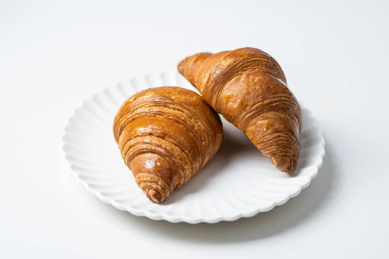 two croissants on a white plate on a table, momoshiki ōtsutsuki, high quality product image”, brown:-2, sakimichan