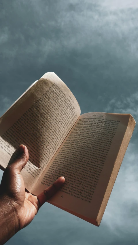 a person holding an open book in the air, by Carey Morris, pexels contest winner, blue sky, plain background, studious chiaroscuro, instagram story