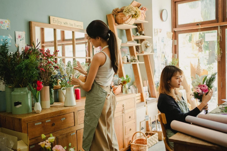 a woman standing next to a woman sitting at a table, trending on pexels, arts and crafts movement, flower shop scene, nanae kawahara, neat and tidy, from the side