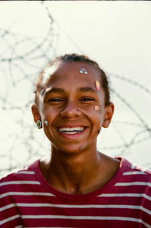 a young girl smiles in front of a barbed wire fence, pexels contest winner, graffiti, cornrows, award winning movie still, ashteroth, teenage boy