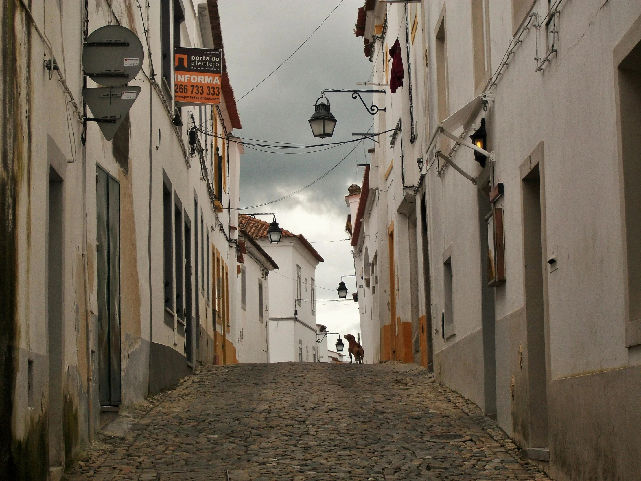 a cobblestone street lined with white buildings, inspired by Almada Negreiros, pexels contest winner, gray sky, square, rural, slide show