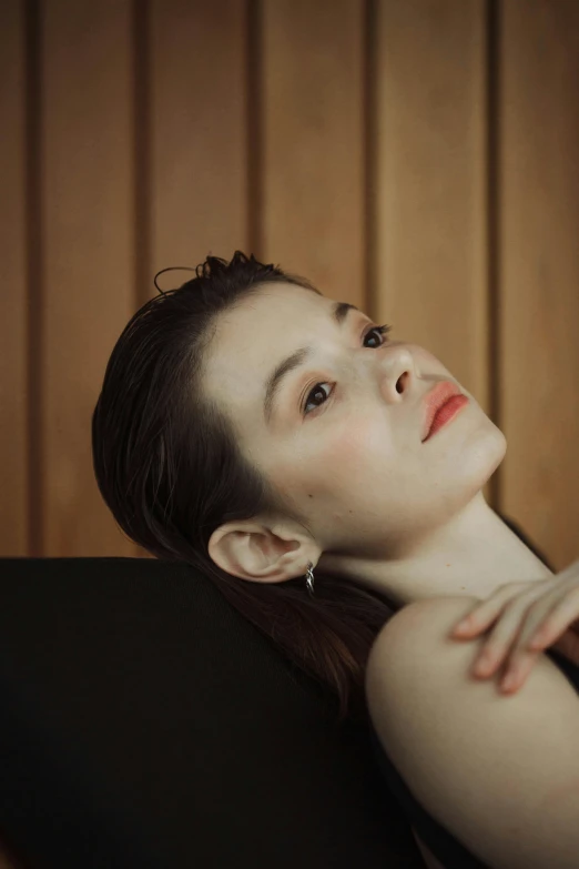 a woman sitting on top of a black chair, inspired by Galen Dara, trending on pexels, hyperrealism, sharp cheekbones, natural soft pale skin, lying down, skincare