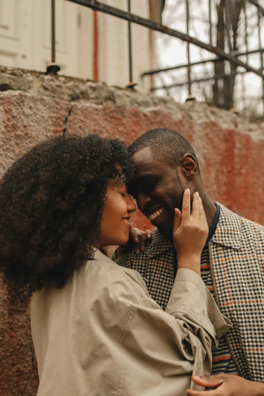 a man and woman standing next to a brick wall, pexels contest winner, natural hair, embracing, hearts, brown skinned