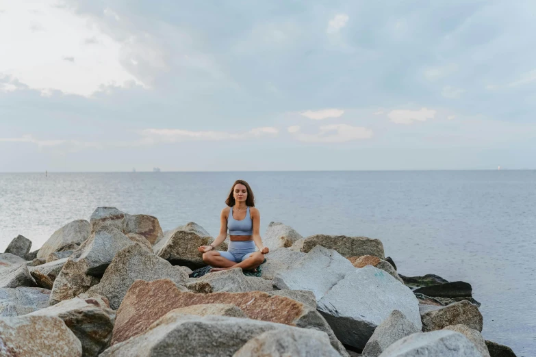 a woman sitting on rocks in front of a body of water, avatar image