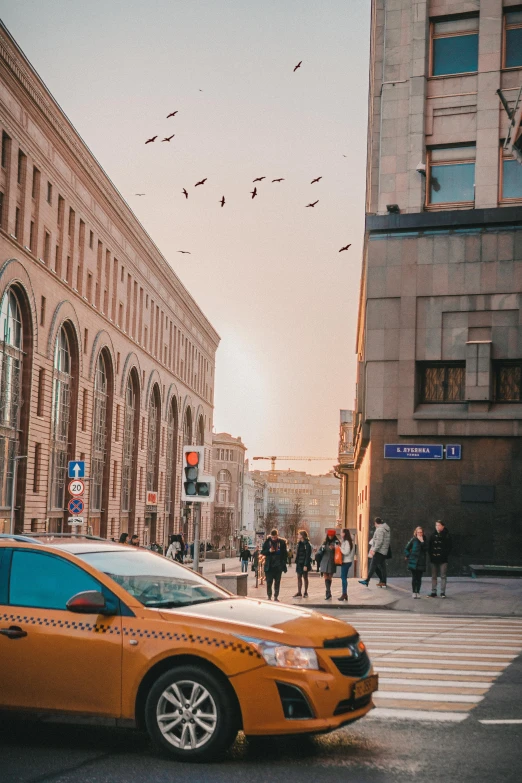 a yellow taxi driving down a street next to tall buildings, a photo, by Adam Marczyński, pexels contest winner, neoclassicism, late afternoon, people on the ground, russian architecture, split near the left