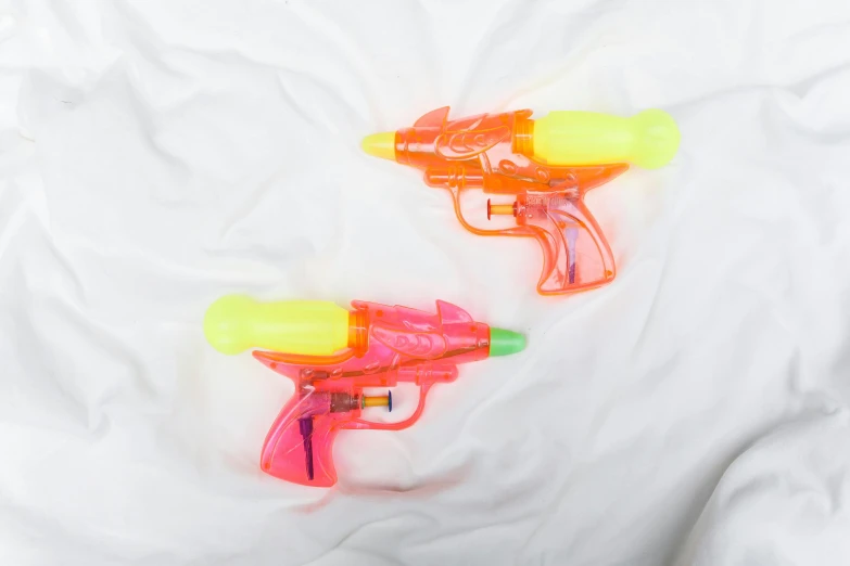 a couple of water guns laying on top of a bed, multi - coloured, mint