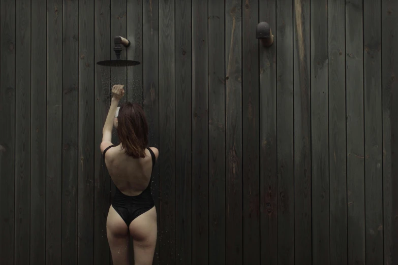 a woman standing in front of a wooden wall, unsplash, conceptual art, showers, hegre, black swimsuit, rear view