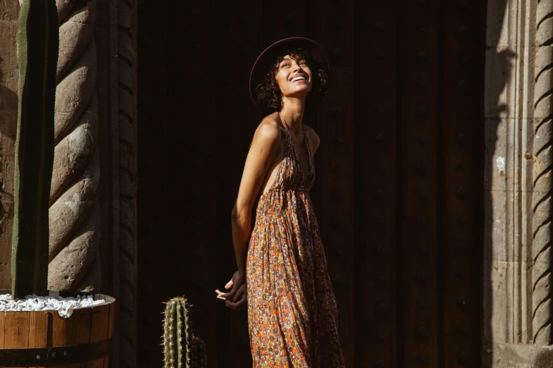 a woman standing in front of a barrel of cacti, inspired by Eva Gonzalès, pexels contest winner, wearing a flowing sundress, caracter with brown hat, smiling fashion model, leaning on door