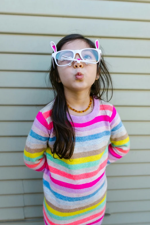 a little girl standing in front of a wall, inspired by Okuda Gensō, pexels contest winner, photorealism, square rimmed glasses, silly playful fun face, stripe over eye, young asian girl