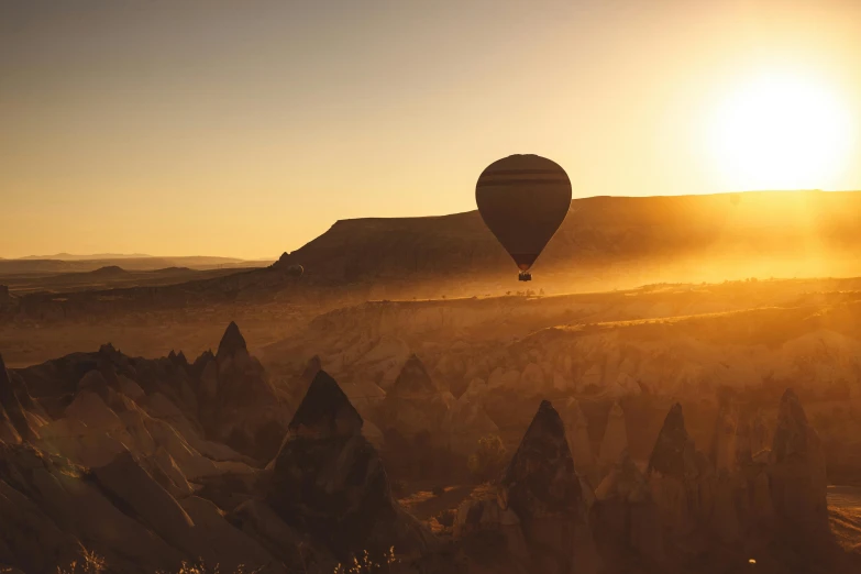 a hot air balloon flying over a valley at sunset, by Peter Churcher, pexels contest winner, sandstone, historical photo, yellow, brown