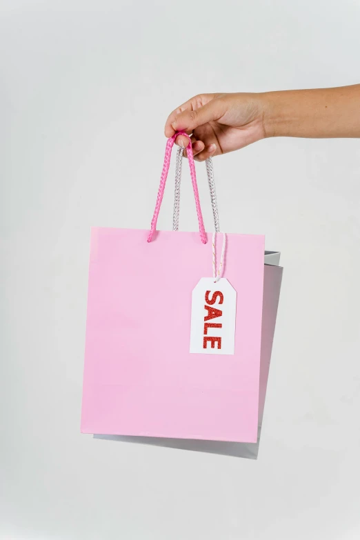 a person holding a pink shopping bag with a sale tag on it, a photo, by Daniel Gelon, square, h 576, f / 1, digital image