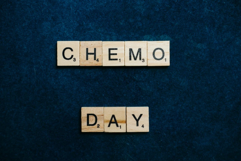 the word chemo day spelled in scrabbles on a blue background, an album cover, chemicals, against dark background, may), a wooden
