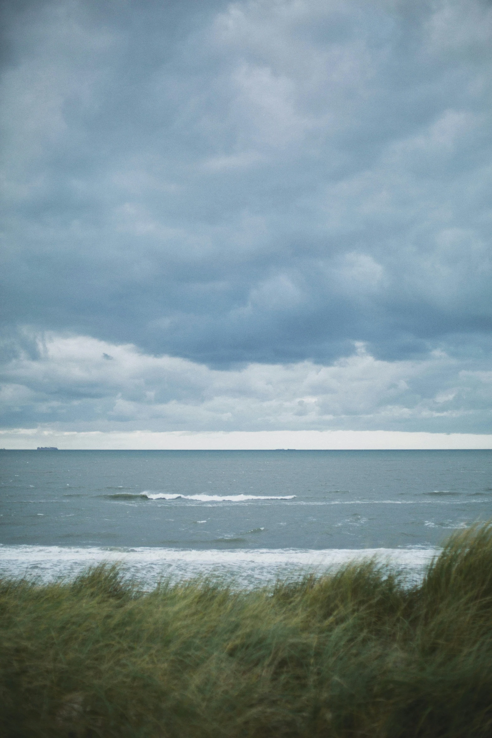 a man riding a surfboard on top of a sandy beach, inspired by Thomas Struth, minimalism, scotland, thunderclouds, hasselblad photograph, muted color (blues