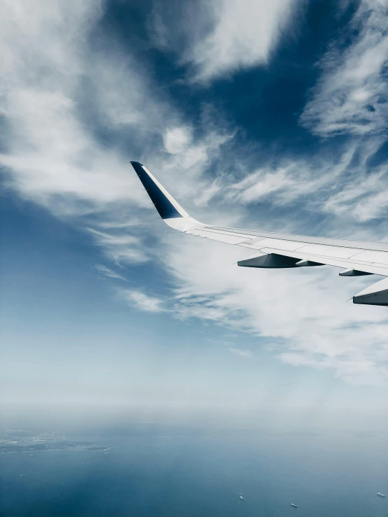 the wing of an airplane flying over a body of water, pexels contest winner, modernism, wispy clouds in a blue sky, thumbnail, profile view perspective, airplanes