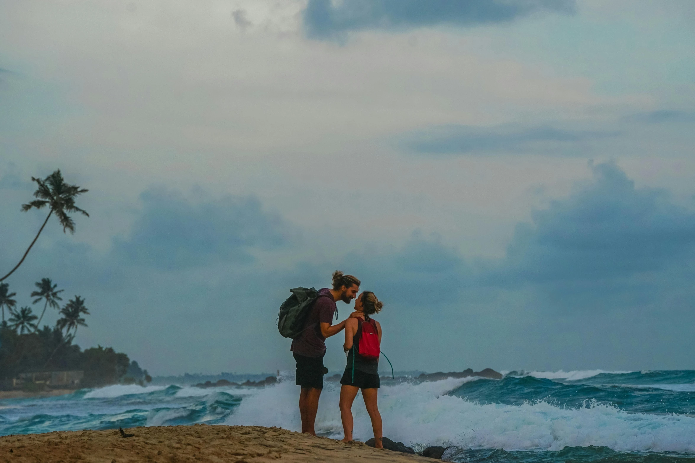 a couple of people standing on top of a sandy beach, a picture, with a backpack, profile image, epic coves crashing waves plants, couple kissing