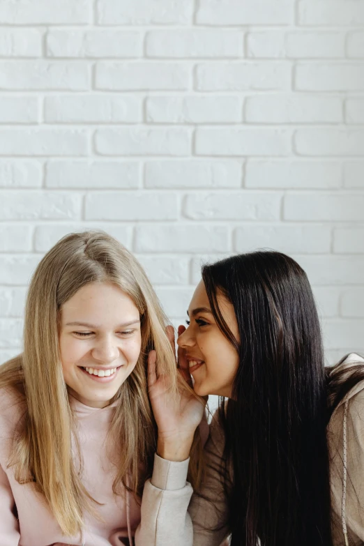 a couple of women sitting on top of a bed next to each other, trending on pexels, happening, earing a shirt laughing, young with long hair, profile pic, on a white table