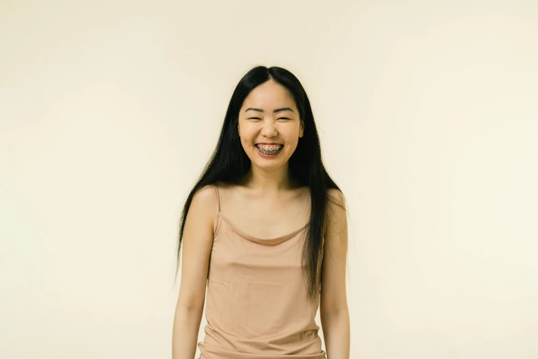 a woman standing in front of a white wall, a character portrait, inspired by Kim Tschang Yeul, pexels contest winner, mingei, earing a shirt laughing, light tan, asian human, wearing a camisole