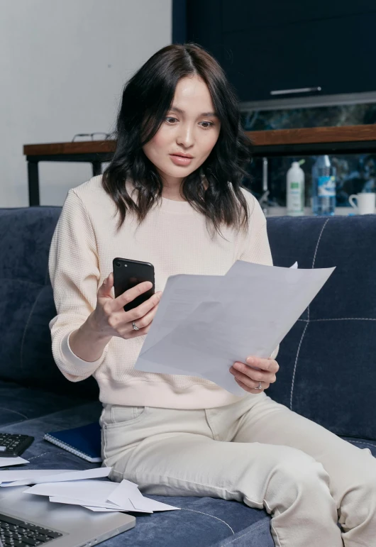 a woman sitting on a couch holding a cell phone, papers, kimi takemura, ceo, wētā fx