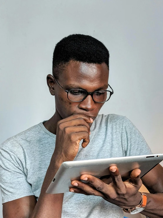 a man in glasses using a tablet computer, pexels, man is with black skin, pondering, gray men, aged 2 5