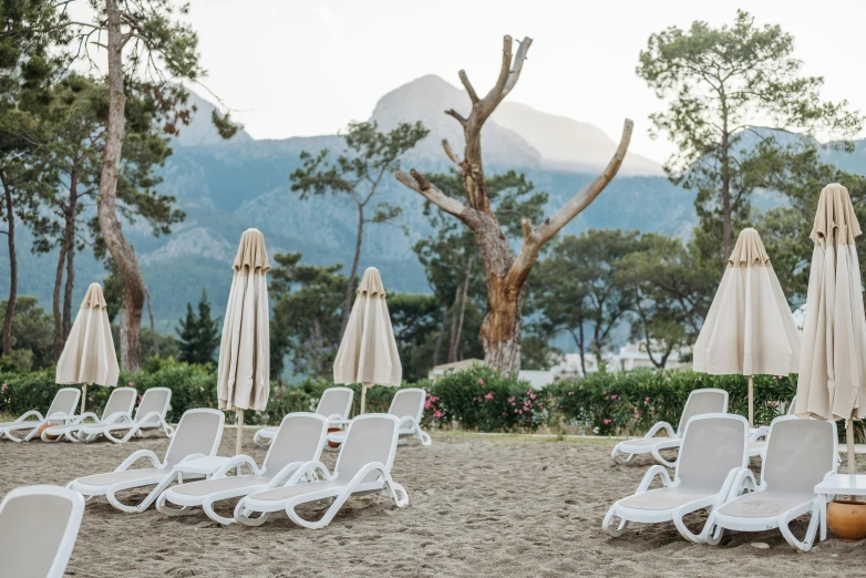 a bunch of lawn chairs and umbrellas on a beach, unsplash, art nouveau, mountains in the background, cypresses, conde nast traveler photo, white