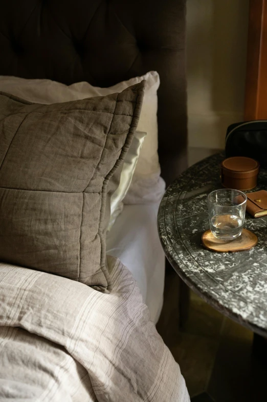 a glass of wine sitting on top of a table next to a bed, inspired by Harriet Backer, featured on pinterest, taupe, middle close up, slate, pillows