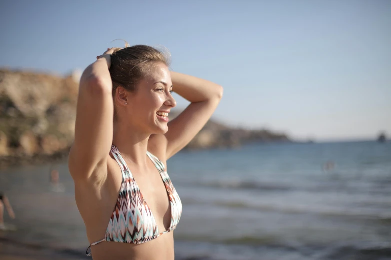 a woman standing on top of a beach next to the ocean, wearing bra, turning her head and smiling, profile image, holiday