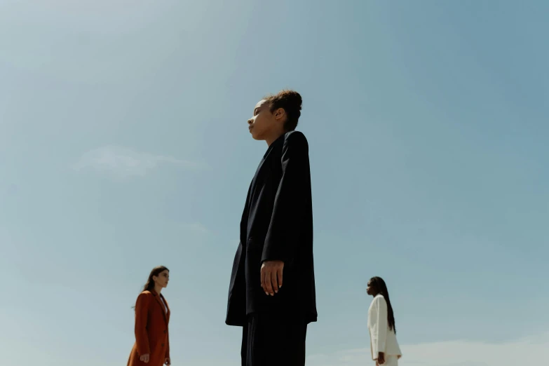 a man standing on top of a beach next to a woman, an album cover, unsplash, bauhaus, three women, wearing black robes, low angle facing sky, ashteroth