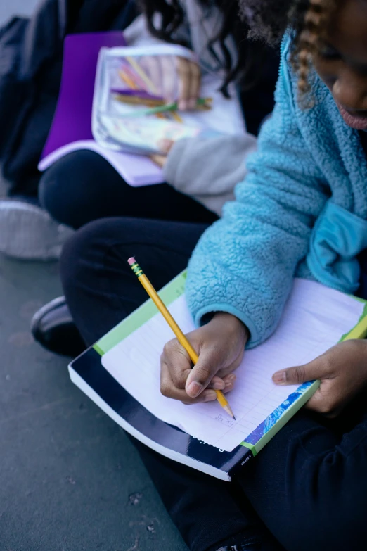 a little girl sitting on the ground with a pencil in her hand, holding notebook, ryan kiera armstrong, ap news, essence