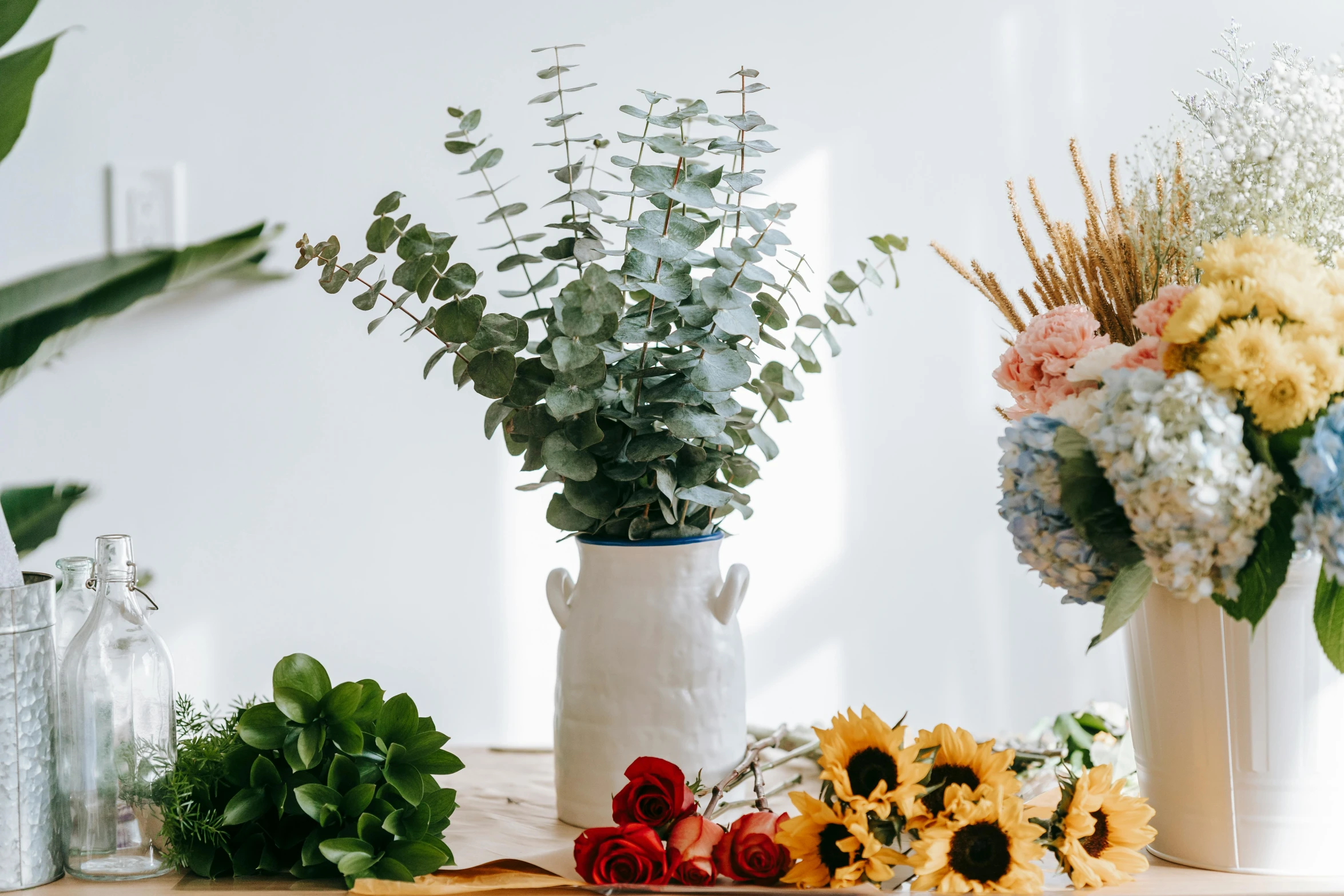 a wooden table topped with vases filled with flowers, a still life, inspired by Eden Box, trending on pexels, eucalyptus, with a white background, vines and blue foliage, various posed