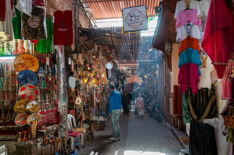 a man walking through a market filled with lots of items, hurufiyya, profile image, moroccan tile archways, thumbnail, warm sunshine