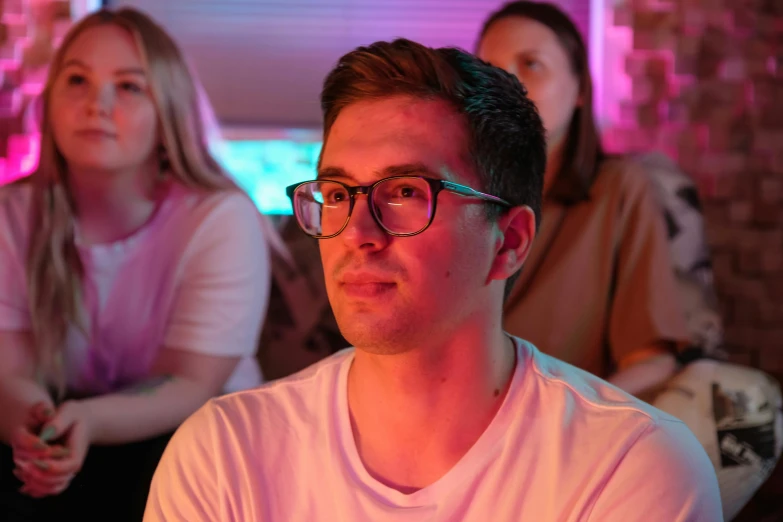 a man with glasses sitting in front of a group of people, bisexual lighting, gaming, cinematic pastel lighting, profile picture 1024px
