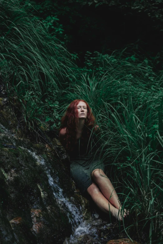 a woman sitting on a rock next to a waterfall, an album cover, inspired by Elsa Bleda, pexels contest winner, renaissance, lush grass, ( redhead, poison ivy, ignant