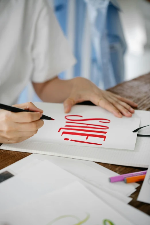 a person sitting at a table writing on a piece of paper, a drawing, trending on pexels, letterism, red and white color theme, professional logo, letter s, handcrafted