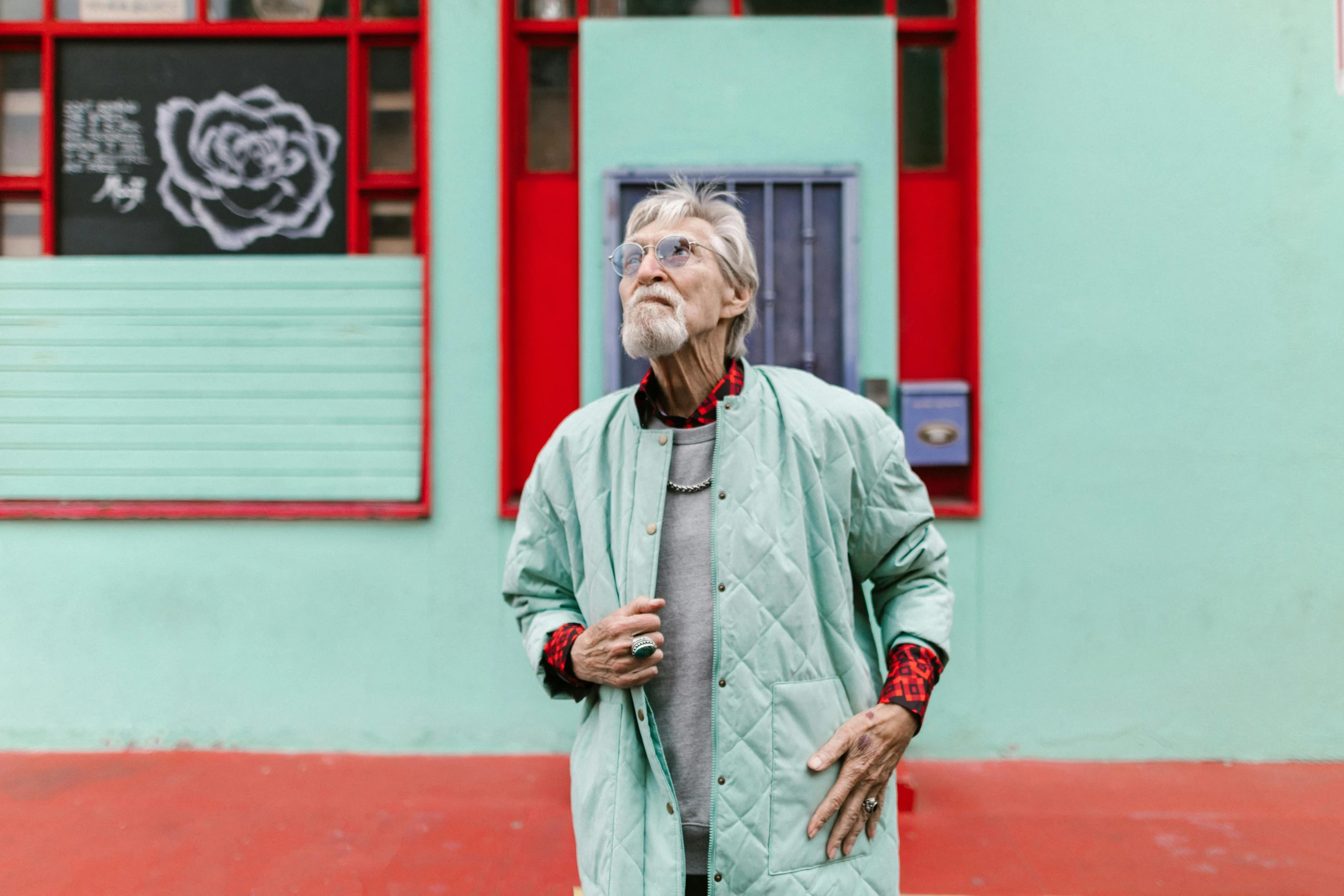 a man standing in front of a green building, inspired by John Bellany, pexels contest winner, hyperrealism, an old lady with red skin, streetwear, oldman with mustach, haeckel and alasdair gray