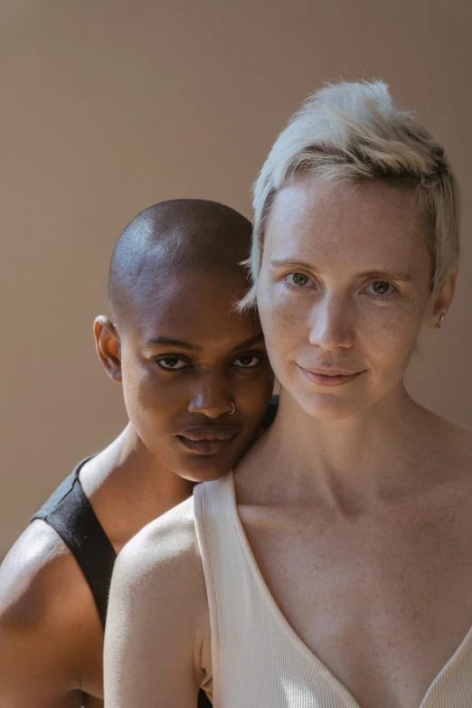 a couple of women standing next to each other, a portrait, by Ellen Gallagher, unsplash, no hair completely bald, cinnamon skin color, nonbinary model, asya yoranova and alan lee