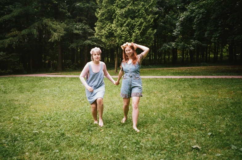 a couple of women standing on top of a lush green field, an album cover, by Attila Meszlenyi, pexels, blue overalls, walking around in forest, concert, 35mm of a very cute