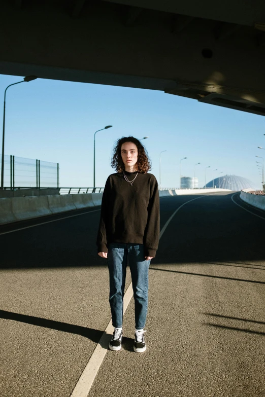 a person standing in the middle of a road, an album cover, pexels contest winner, antipodeans, wearing a black sweater, overpass, uniform off - white sky, curly haired