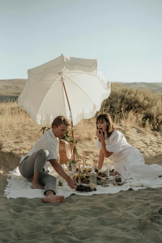 a couple having a picnic on the beach, a portrait, by Jessie Algie, unsplash, land art, idaho, parasol, white robes, dessert