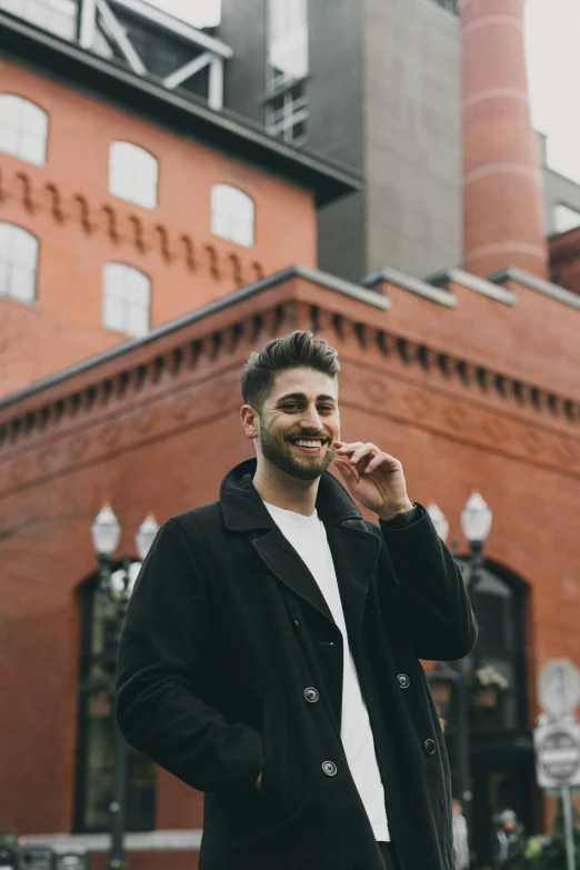 a man standing in front of a brick building talking on a cell phone, a photo, inspired by Anthony Angarola, trending on pexels, smiling :: attractive, h3h3, smiling coyly, tocchini