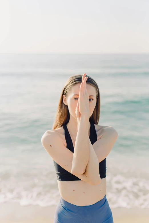 a woman doing a yoga pose on the beach, an album cover, unsplash, hands shielding face, sydney sweeney, low quality photo, plain background