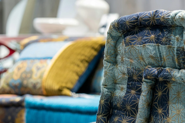 a close up of a chair with a bunch of pillows, inspired by William Morris, unsplash, arts and crafts movement, blue gold suit, chairs and tables, mixed materials, arabian nights inspired